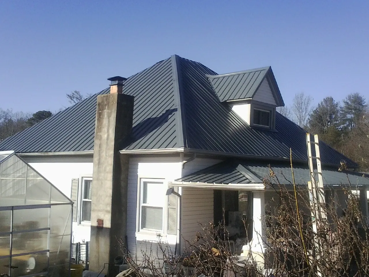 Dark blue standing seam metal roof on a white farmhouse with dormer — Slate & Tile Roof Repair by Roofing Brothers in Gloversville