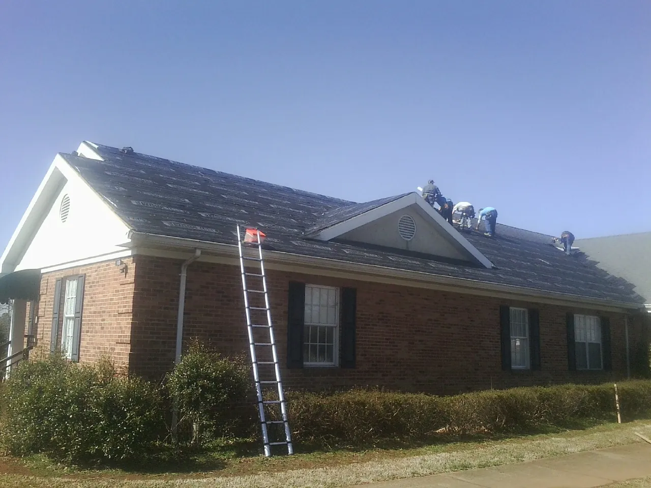 Crew tearing shingles off a brick ranch roof with a ladder set — Metal Roof Repair work by our crew in Gloversville