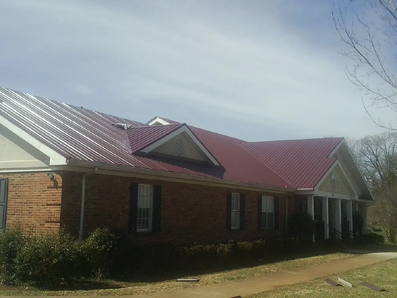 Red metal roof with gabled entries on a long brick building, from a Hail Damage Roof Repair job in Gloversville