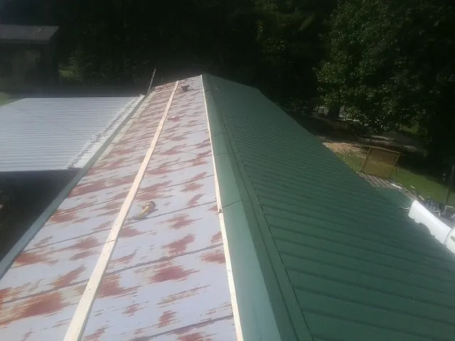 Old rusted panels beside newly installed green metal roofing — Wind Damage Roof Repair by Roofing Brothers in Gloversville