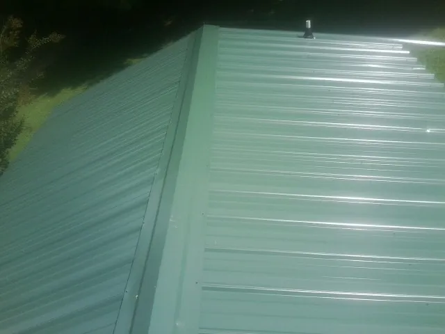 New green metal panels meeting at the ridge of a roof — Flat Roof Repair work by our crew in Gloversville