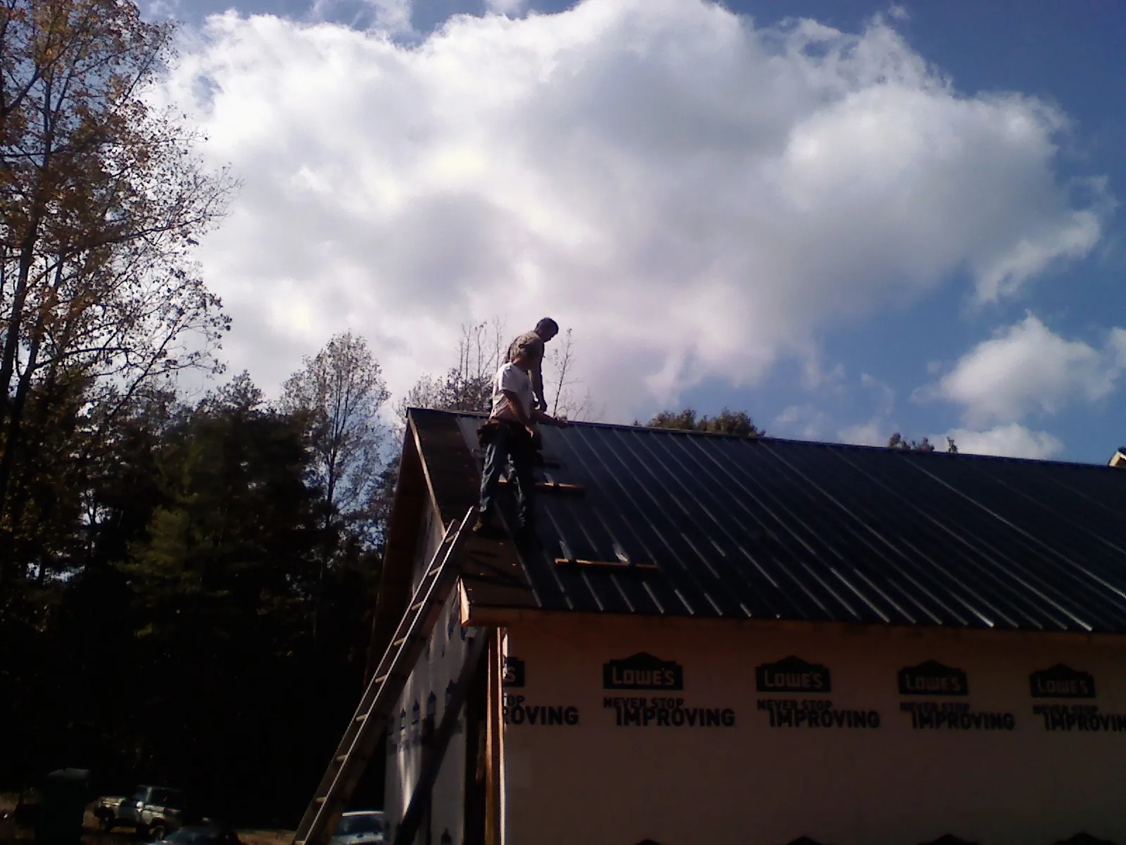 Roofer fastening dark metal panels high against a cloudy sky, from a Roof Inspection job in Gloversville