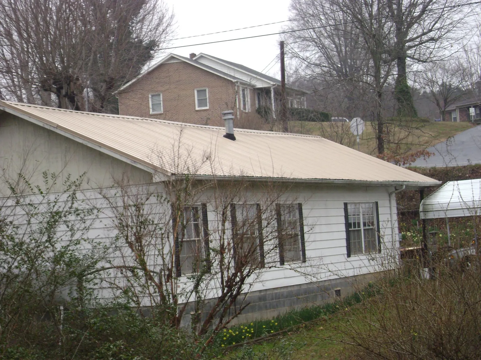 Tan metal roof on a white sided house set into a hillside — Commercial Roofing by Roofing Brothers in Gloversville