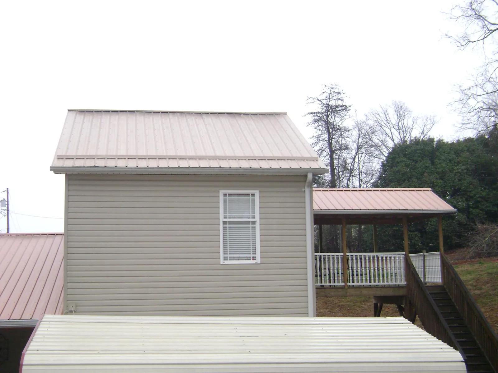 Tan metal roofs on a two story addition and attached porch, from a Roof Replacement job in Gloversville